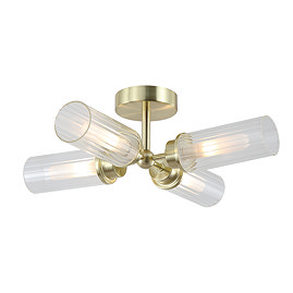 A satin brass four‑light flush ceiling fitting with four ribbed glass cylinders arranged in a cross shape, each glowing warmly.