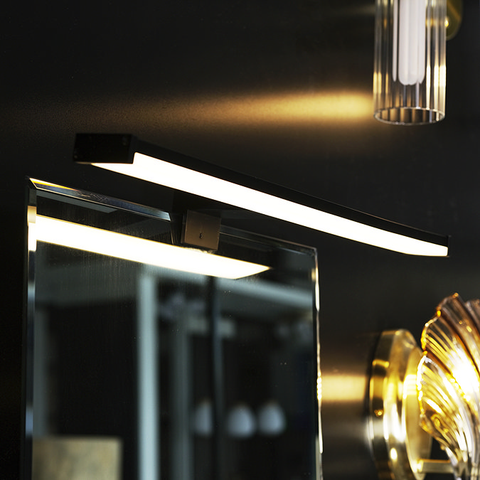A slim black LED mirror light mounted at the top edge of a bathroom mirror, casting bright downward illumination in a dark, modern interior.