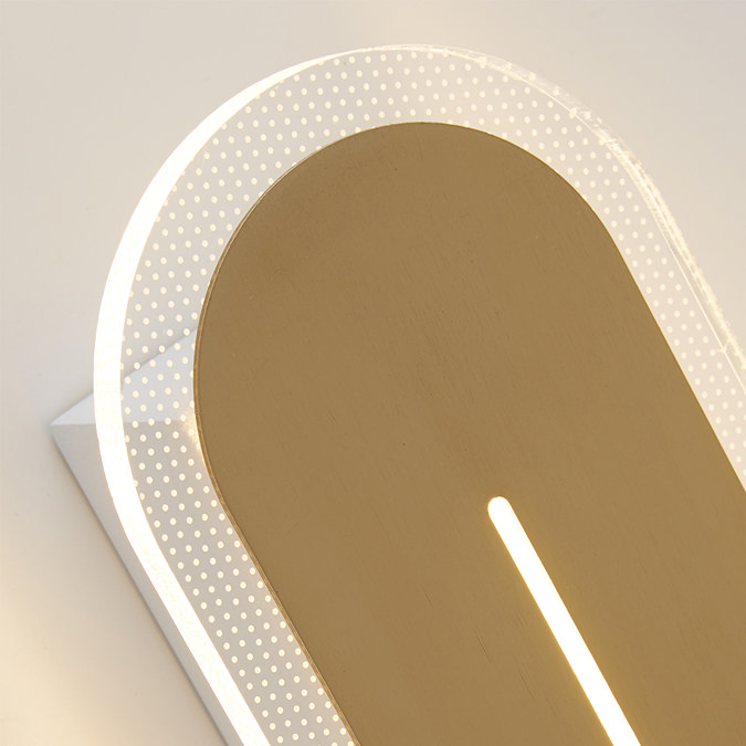 Close‑up of the satin‑brass wall light showing the glowing vertical slit and the dotted clear acrylic border illuminated around the edges.