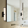 Two tall matt black clamp‑style wall lights with glowing ribbed opal glass tubes mounted on either side of a large bathroom mirror above a modern sink.