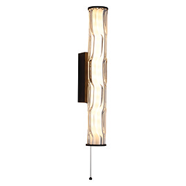 A tall matt black wall light with a glowing wave‑ridged glass diffuser and a pull‑cord hanging from the bottom.