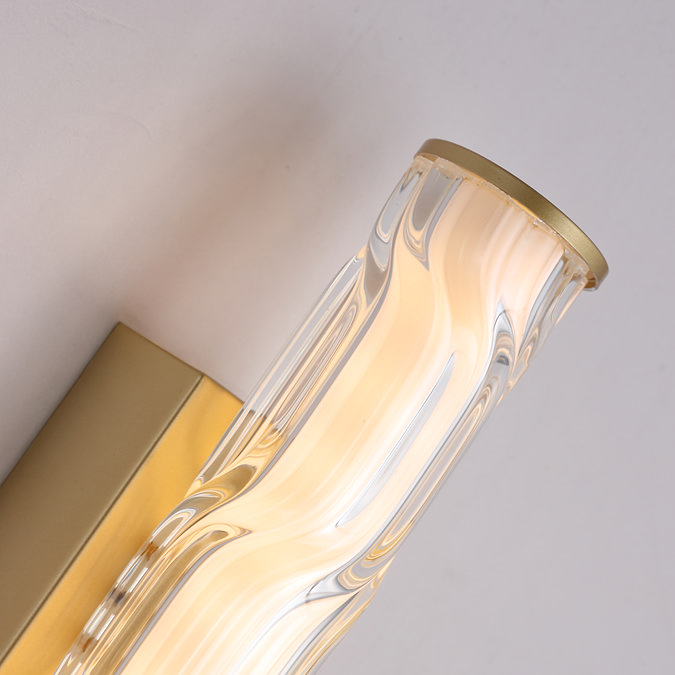 Close‑up of the wall light showing the curved wave‑ridged glass diffuser, the matt gold backplate, and the matt gold end cap illuminated from within.