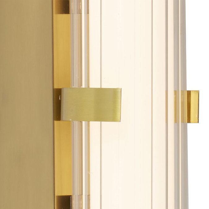 Close‑up of the gold clamp wall light showing the glowing ribbed opal glass tube and the gold metal clamp securing it at the centre.