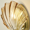 Close‑up of the ribbed amber glass shade and satin brass backplate of the scallop‑shaped wall light, shown glowing warmly.