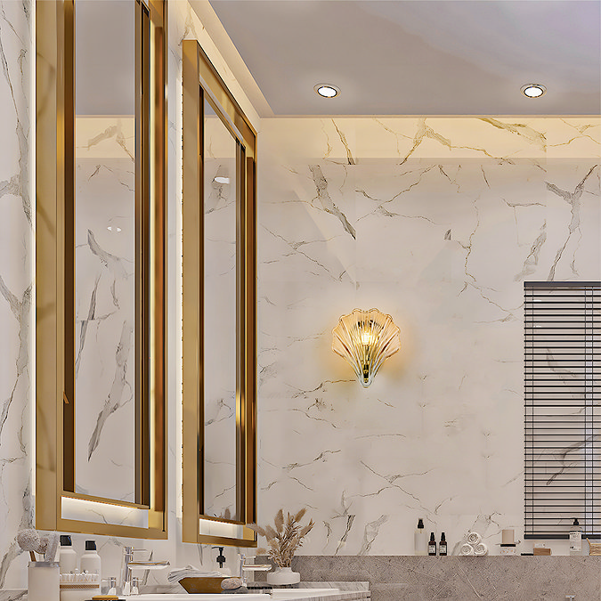 A scallop‑shaped amber glass wall light mounted on a marble‑effect bathroom wall, casting a warm glow beside a vanity area.