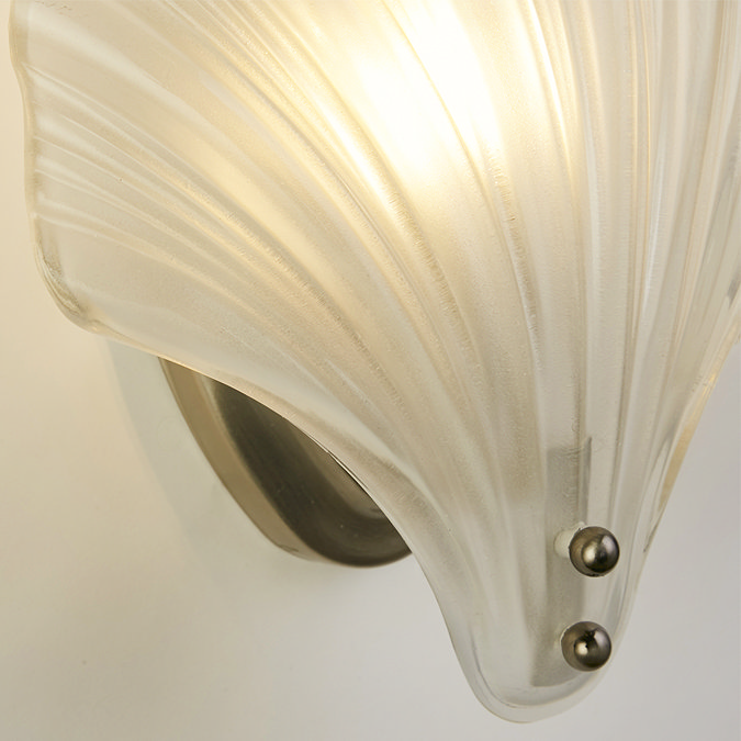 Close‑up of the ribbed frosted glass shade and satin silver backplate of the scallop‑shaped wall light, shown glowing.