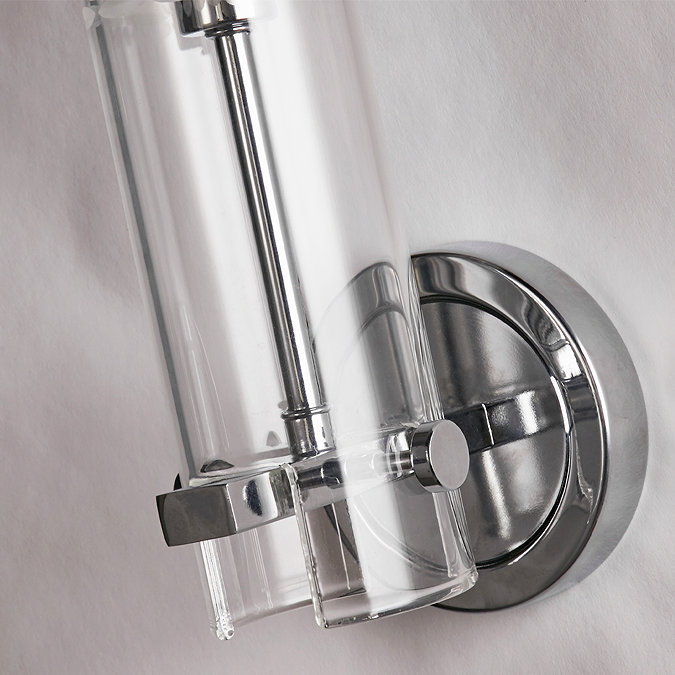 Close‑up view of the chrome wall plate and the lower section of the clear cylindrical glass shade of the bathroom wall light.