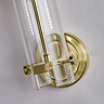 Close‑up view of the satin brass wall plate and the lower section of the clear cylindrical glass shade of the bathroom wall light.