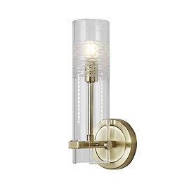 A satin brass bathroom wall light with a cylindrical clear glass shade featuring a frosted etched pattern near the top, shown illuminated.