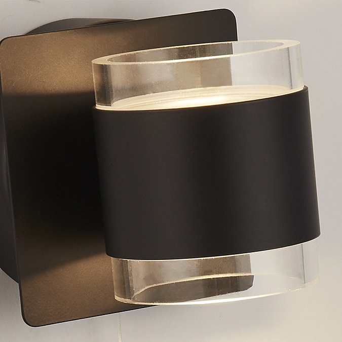 Close‑up of the matt black up‑and‑down wall light showing the clear acrylic cylinder that diffuses light above and below.