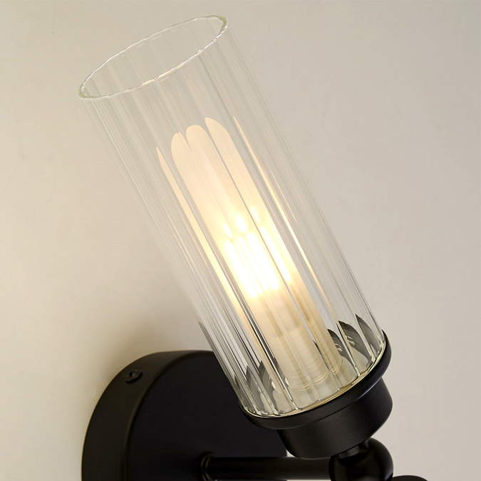Close‑up of the upper ribbed glass shade of the matt black up‑and‑down wall light, showing warm illumination inside the glass.