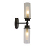 A matt black up‑and‑down wall light with two clear ribbed glass shades, each glowing softly to show the light is switched on.