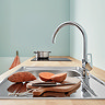 Grohe StartLoop chrome C-spout kitchen mixer tap installed in a stainless steel sink within a modern kitchen setting.