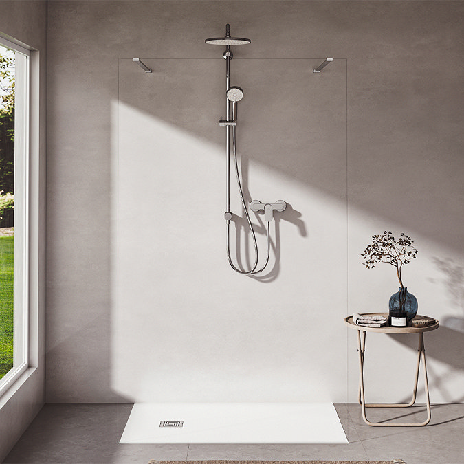 The Ideal Standard Ceratwist T25 Exposed Shower Kit with Fixed Head & Handset - 8 l/min fixed in a modern bathroom with beige tile walls. There is a large window to the left casting sunlight and shadows into the room.