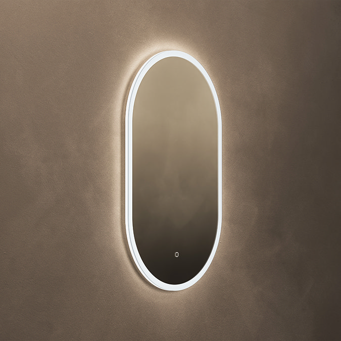 The Roxbury Illuminated Capsule Mirror pictured on a plain beige wall, showing the mirror omitting a bright, cool glow.