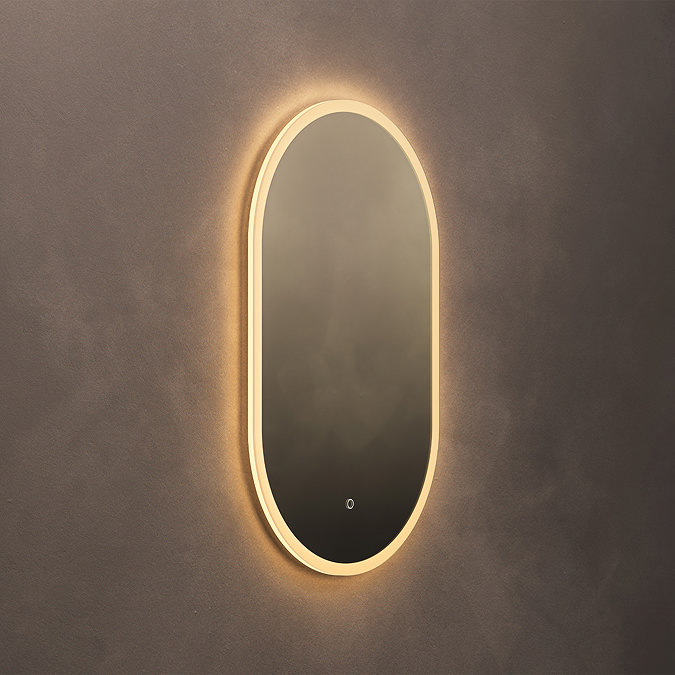 The Roxbury Illuminated Capsule Mirror pictured on a plain beige wall, showing the mirror omitting a warm glow.