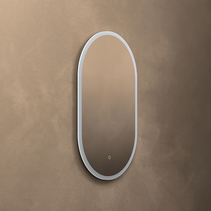 The Roxbury Illuminated Capsule Mirror pictured on a plain beige wall, showing the mirror light turned off.