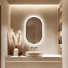 The Roxbury 500 x 800mm Illuminated Capsule Mirror pictured in a beige, modern bathroom, mounted over a beige counter-top basin.