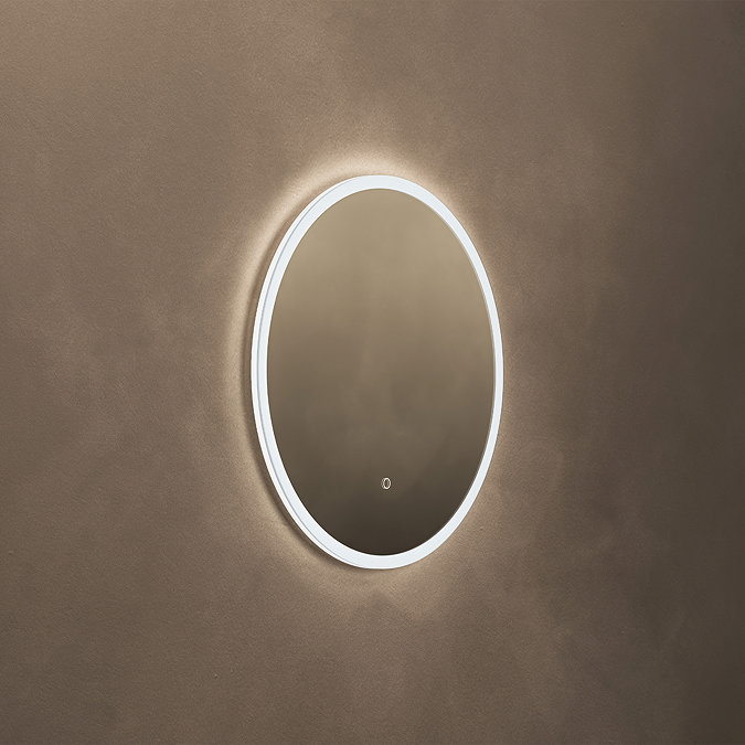 The Roxbury Illuminated Round Mirror pictured on a plain beige wall, showing the mirror omitting a bright, cool glow.