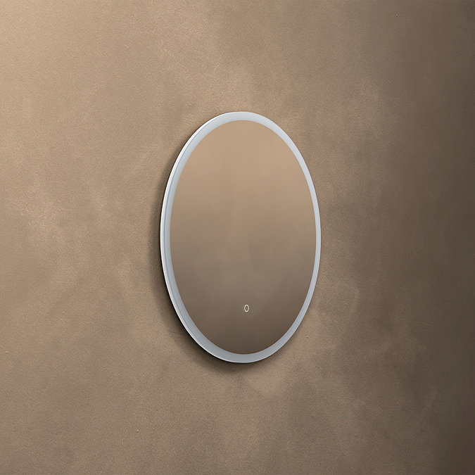The Roxbury Illuminated Round Mirror pictured on a plain beige wall, showing the mirror light turned off.