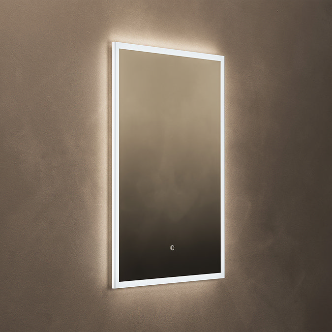 The Roxbury 600 x 800mm Illuminated Rectangular Mirror with Demister Pad pictured on a plain beige wall, showing the mirror omitting a bright, cool glow.